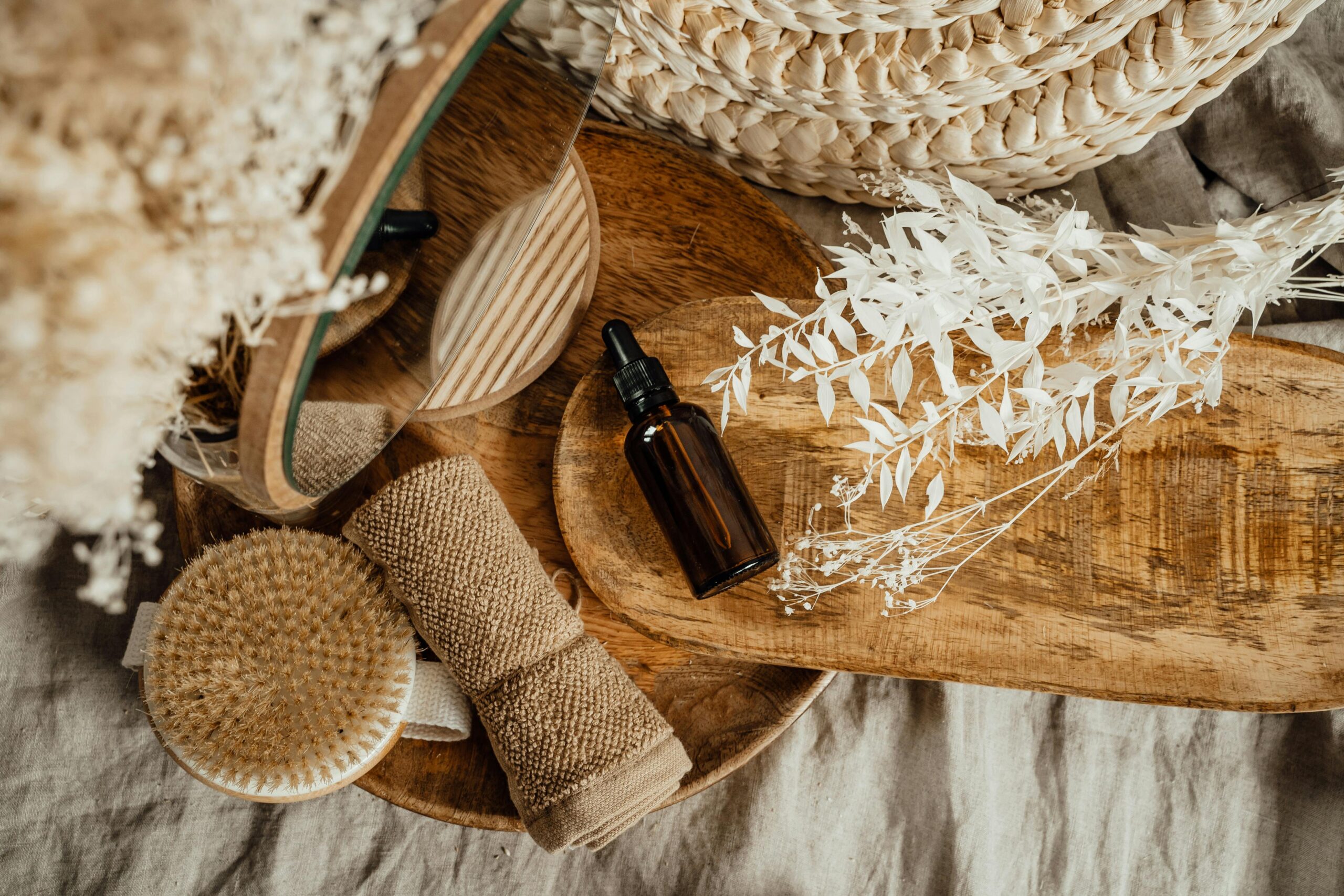 Stylish flat lay of a glass cosmetic bottle on a wooden tray with spa items and dried flowers.